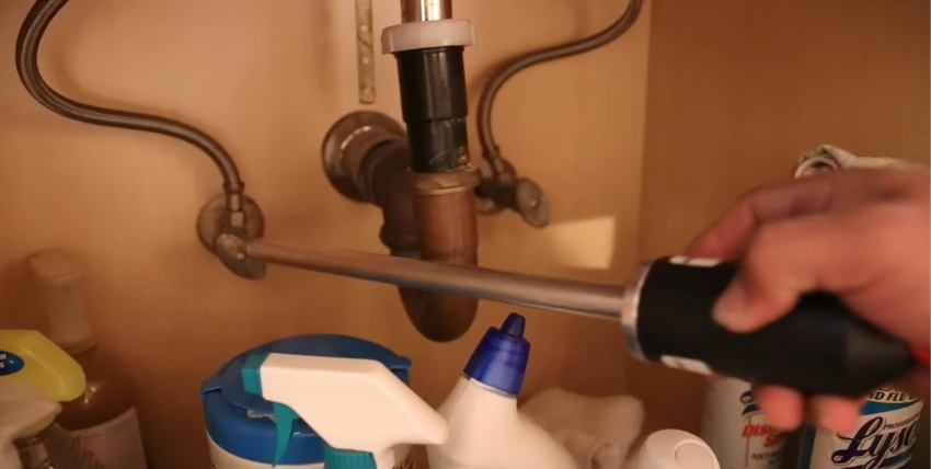 Technician inspecting plumbing beneath a sink for a hidden leak
